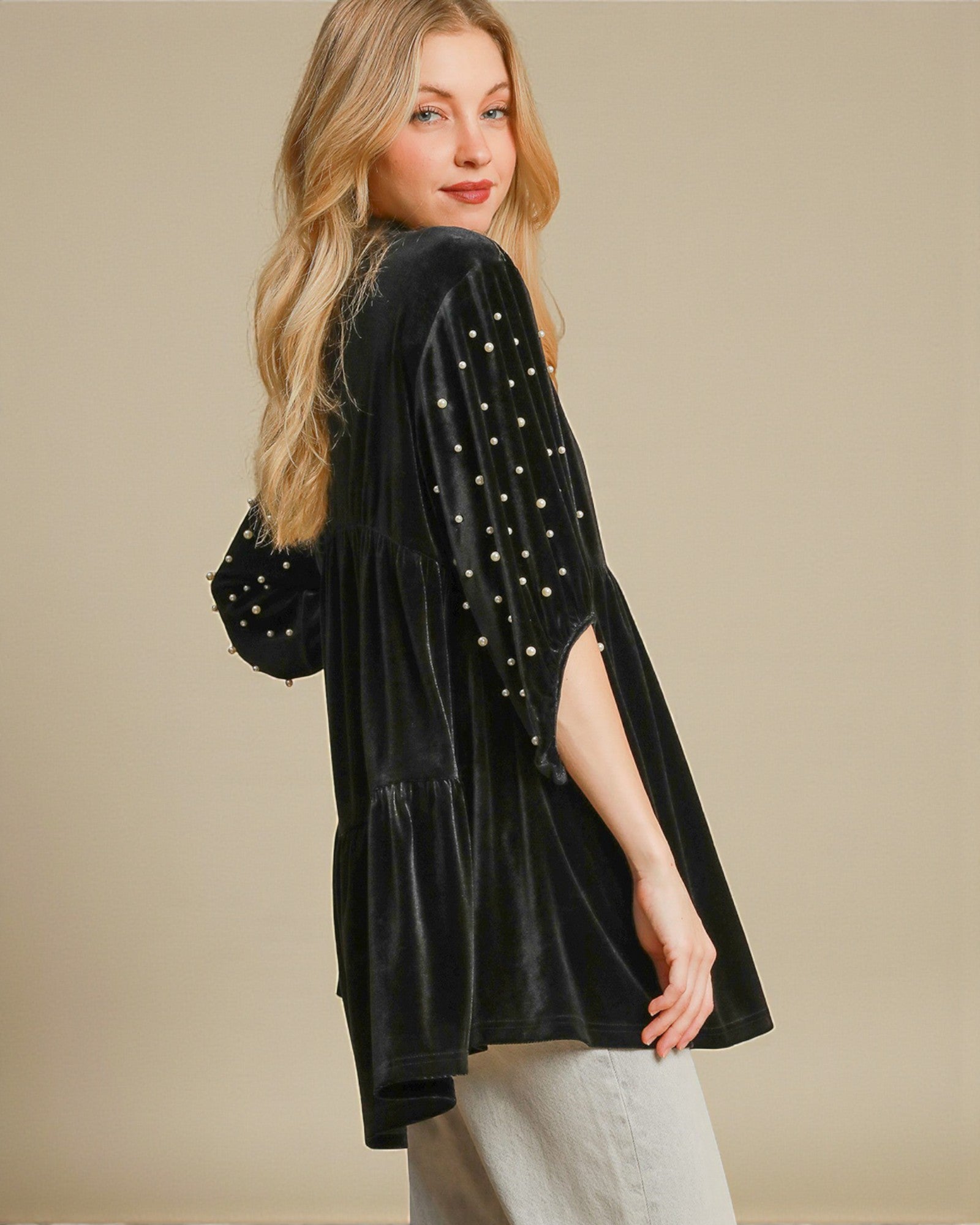 Woman wearing a black velvet kimono with pearl embellishments on a beige background