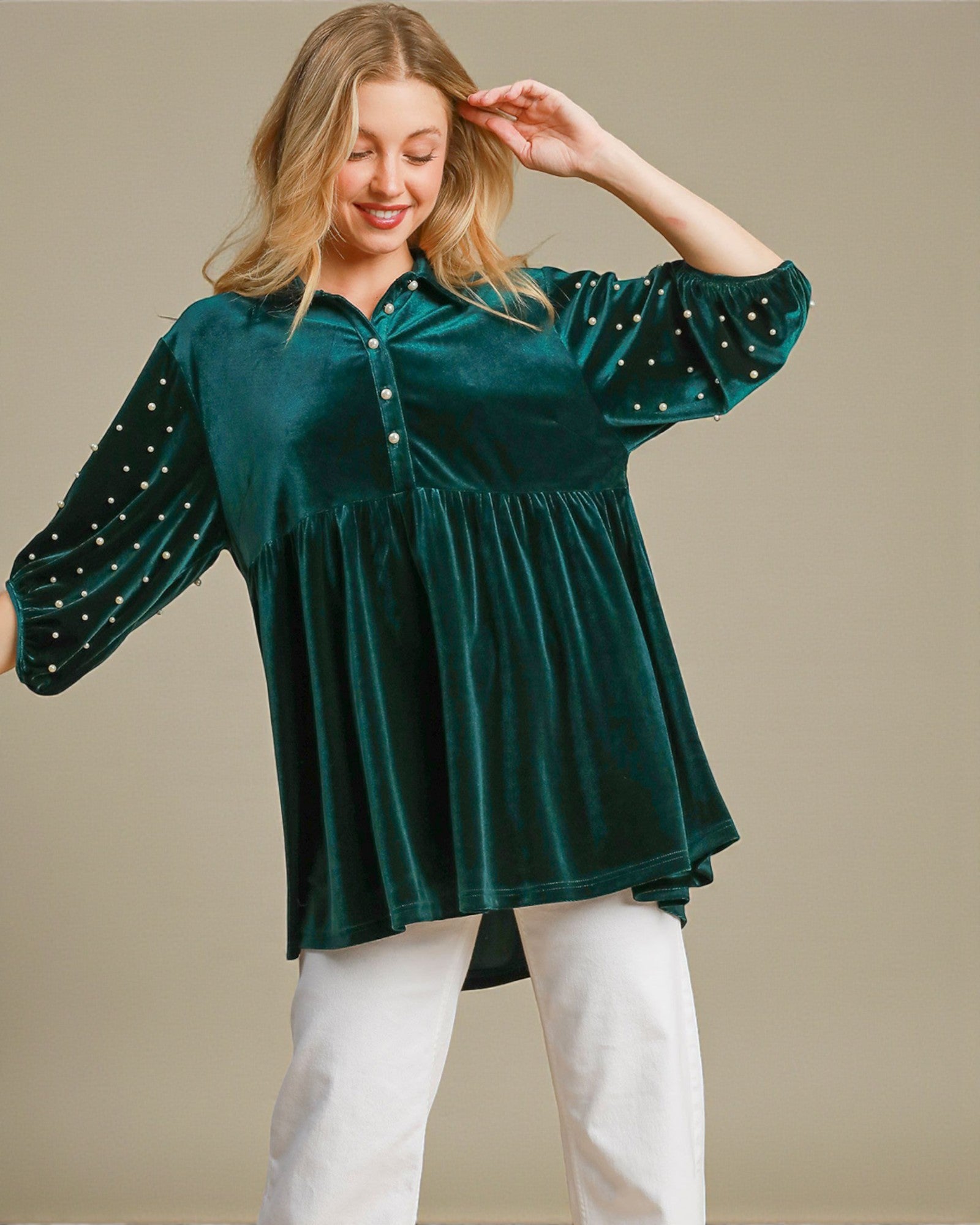 Woman wearing a green velvet blouse with embellished sleeves against a beige background