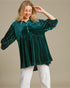 Woman wearing a green velvet blouse with embellished sleeves against a beige background