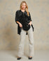 Woman wearing a black blouse with star patterns and light gray pants against a beige background
