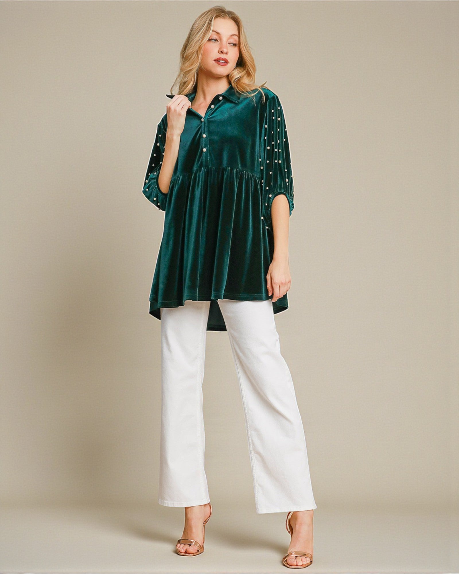 Woman wearing a green velvet top with embellishments and white pants on a beige background