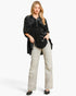 A woman modeling a black velvet long-sleeve top with silver rhinestone embellishments on the sleeves, paired with light beige straight-leg jeans and black pointed flats, against a plain white studio background.