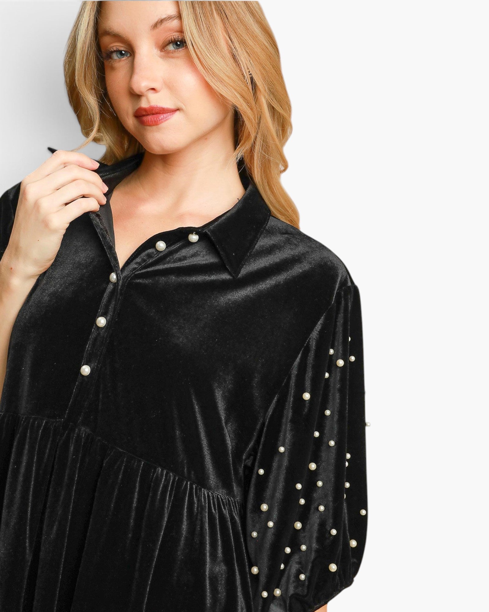 A woman wearing a black velvet long-sleeve blouse with pearl embellishments on the sleeves and a pearl-button placket, shown against a light gray studio background.