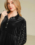 Woman wearing a black velvet dress with pearl embellishments against a neutral background