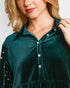 A close-up of a woman wearing a dark teal green velvet button-up blouse with pearl-like decorative buttons and pearl embellishments on the collar and sleeve cuffs.