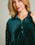 Woman wearing a green velvet dress with pearl buttons against a neutral background