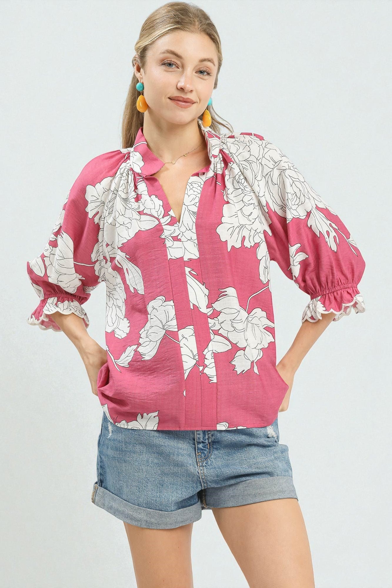 Woman wearing a pink floral blouse and denim shorts on a white background