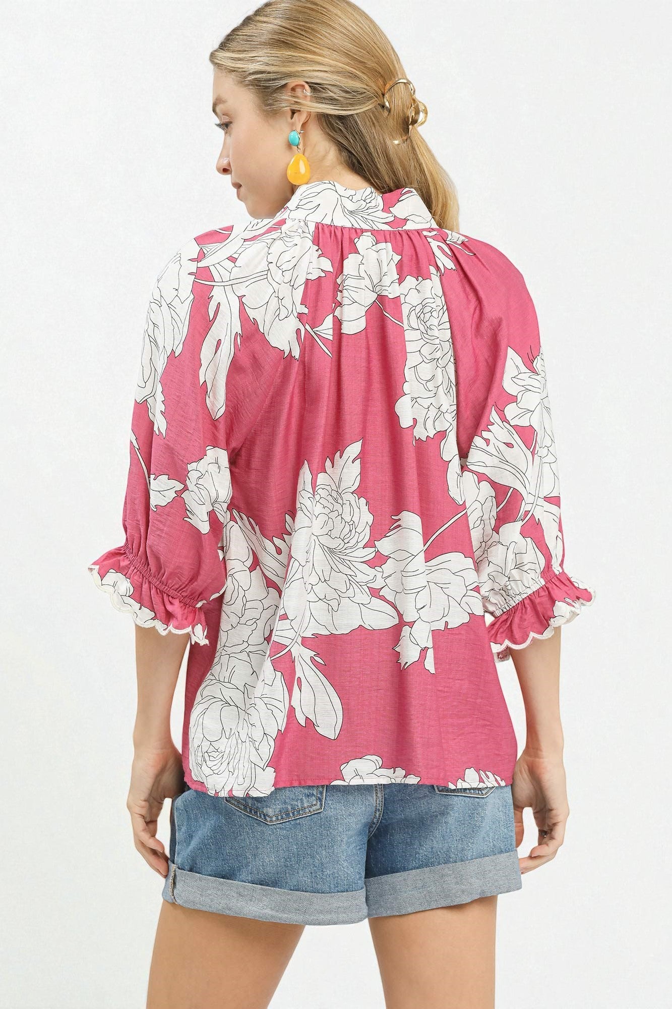 Woman wearing a pink floral blouse with white flowers on a plain background