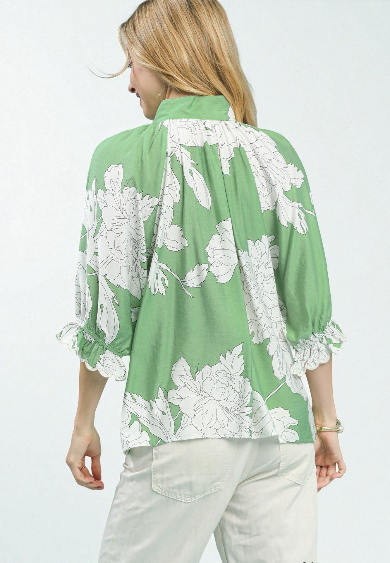 Woman wearing a green blouse with white floral patterns on a plain background