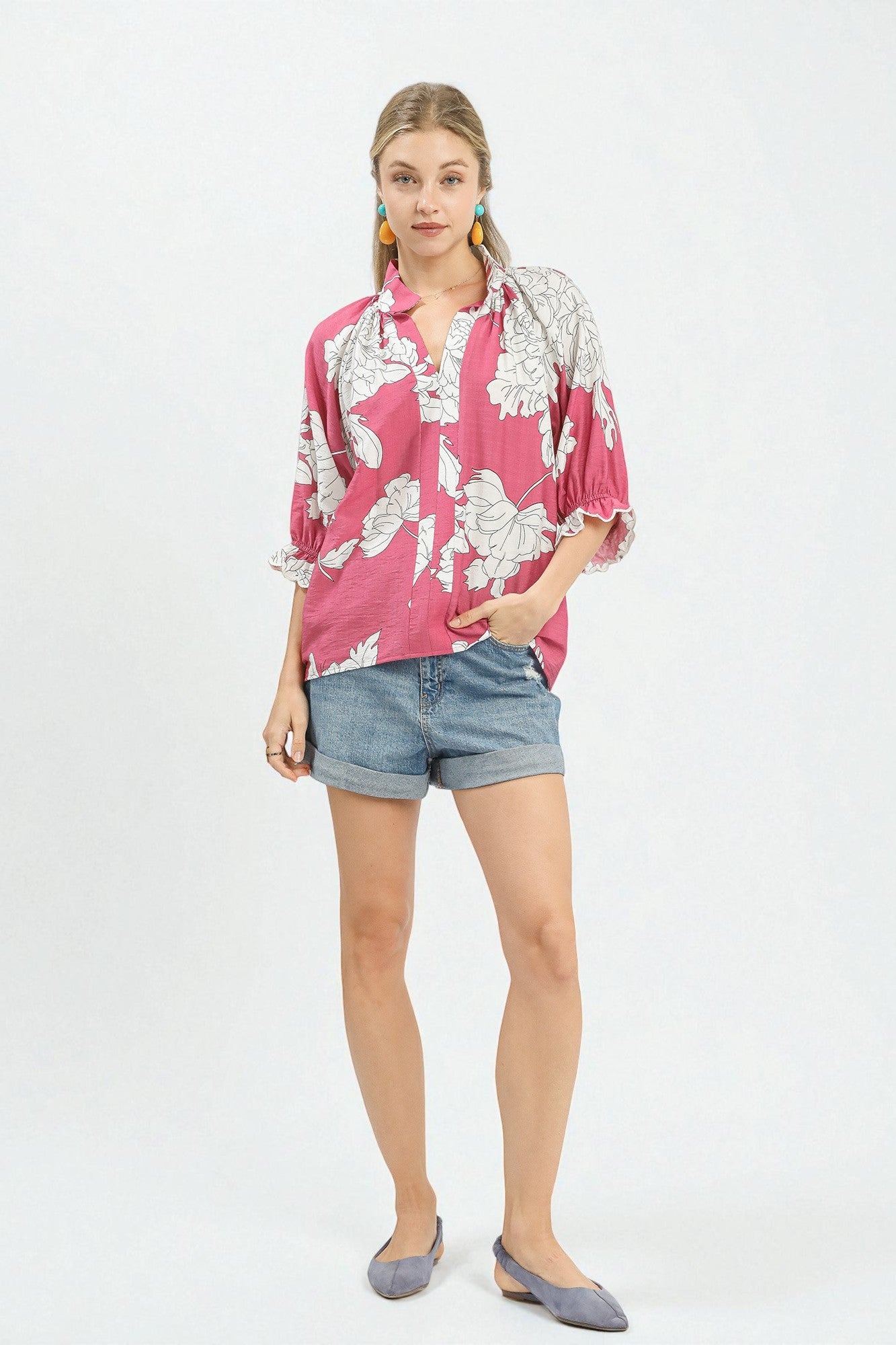 Woman wearing a pink floral blouse and denim shorts on a white background
