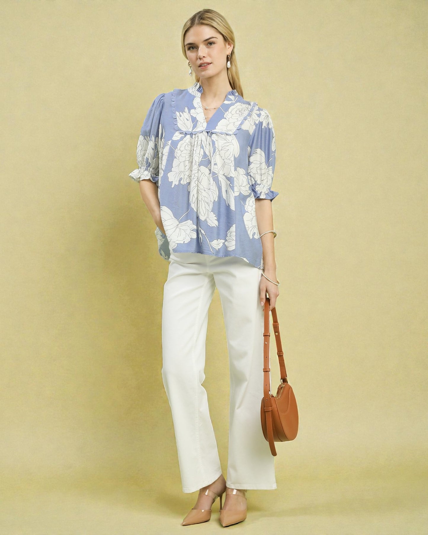 Woman wearing a blue floral blouse and white pants with a brown handbag on a beige background
