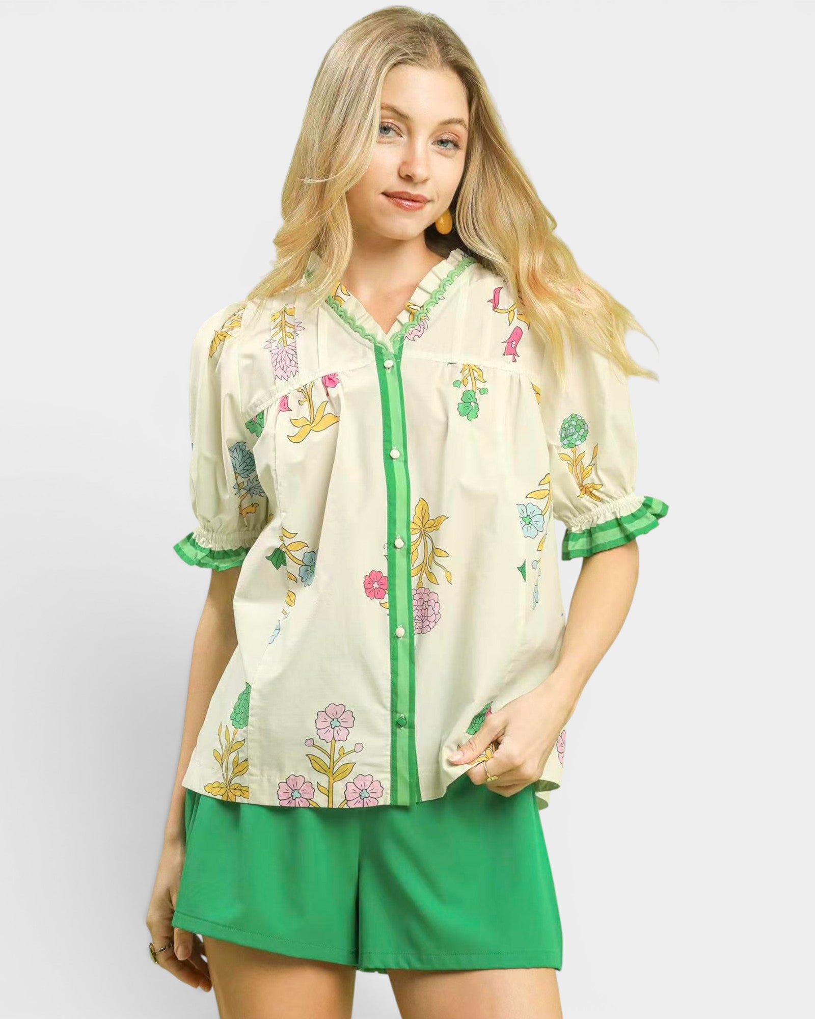 Woman wearing a cream blouse with floral embroidery and green shorts on a white background
