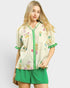 Woman wearing a cream blouse with floral embroidery and green shorts on a white background
