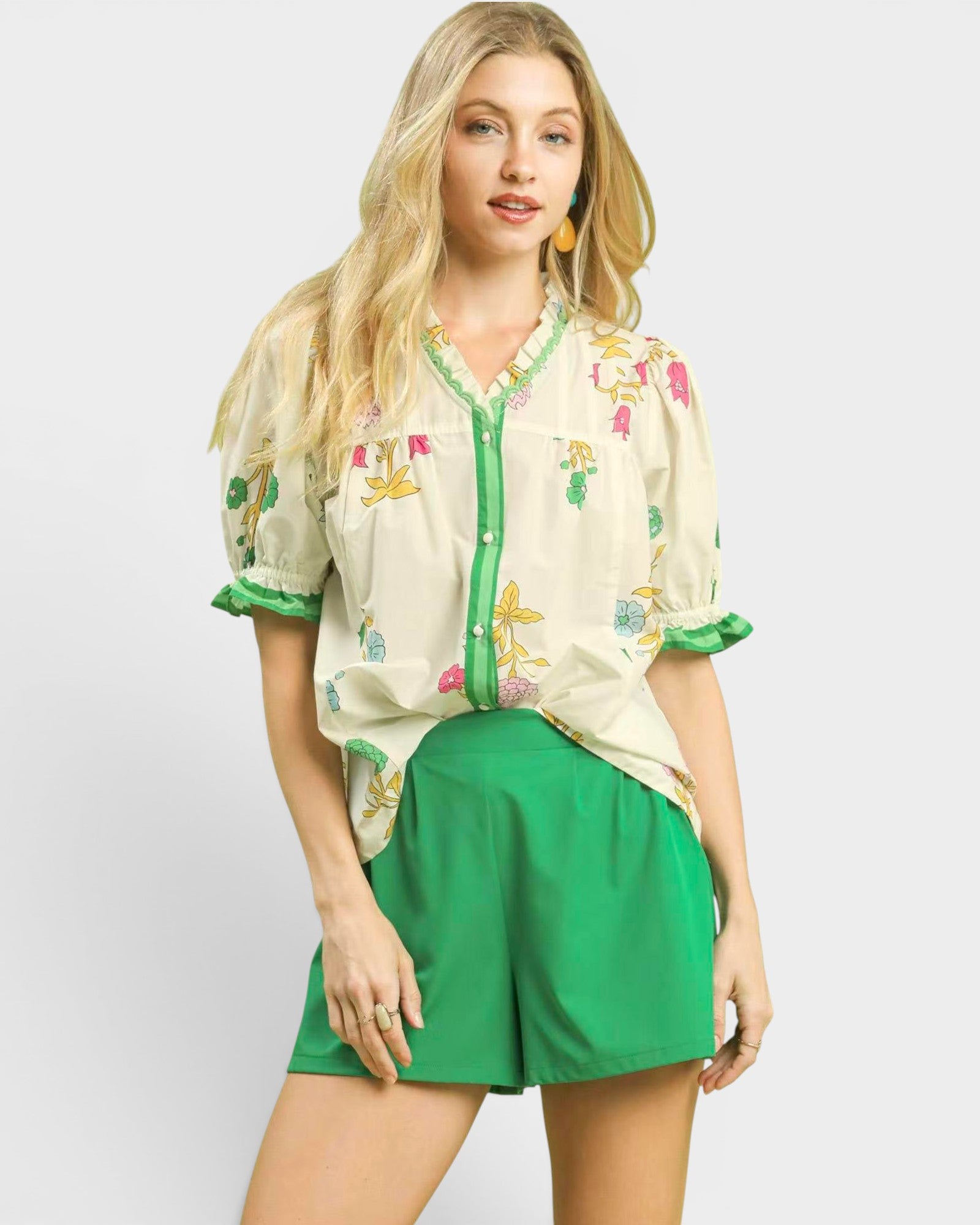 Woman wearing a floral embroidered top and green shorts on a white background