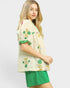 Woman wearing a cream-colored embroidered top with green trim and green shorts on a white background