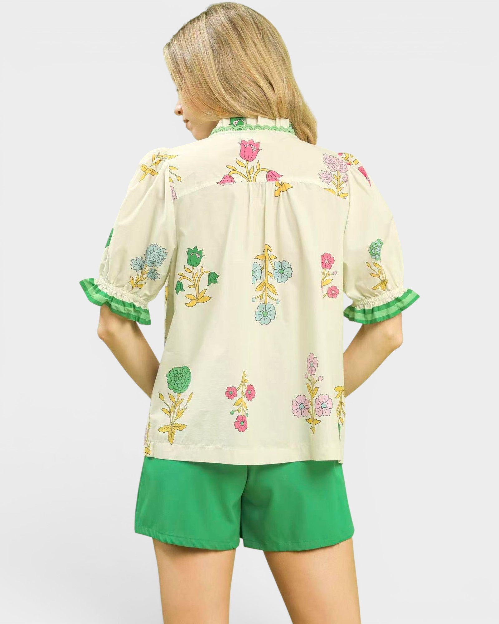 Woman wearing a cream-colored blouse with floral embroidery and green shorts on a white background