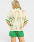 Woman wearing a cream-colored blouse with floral embroidery and green shorts on a white background