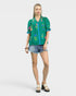 Woman wearing a green embroidered blouse and denim shorts on a white background
