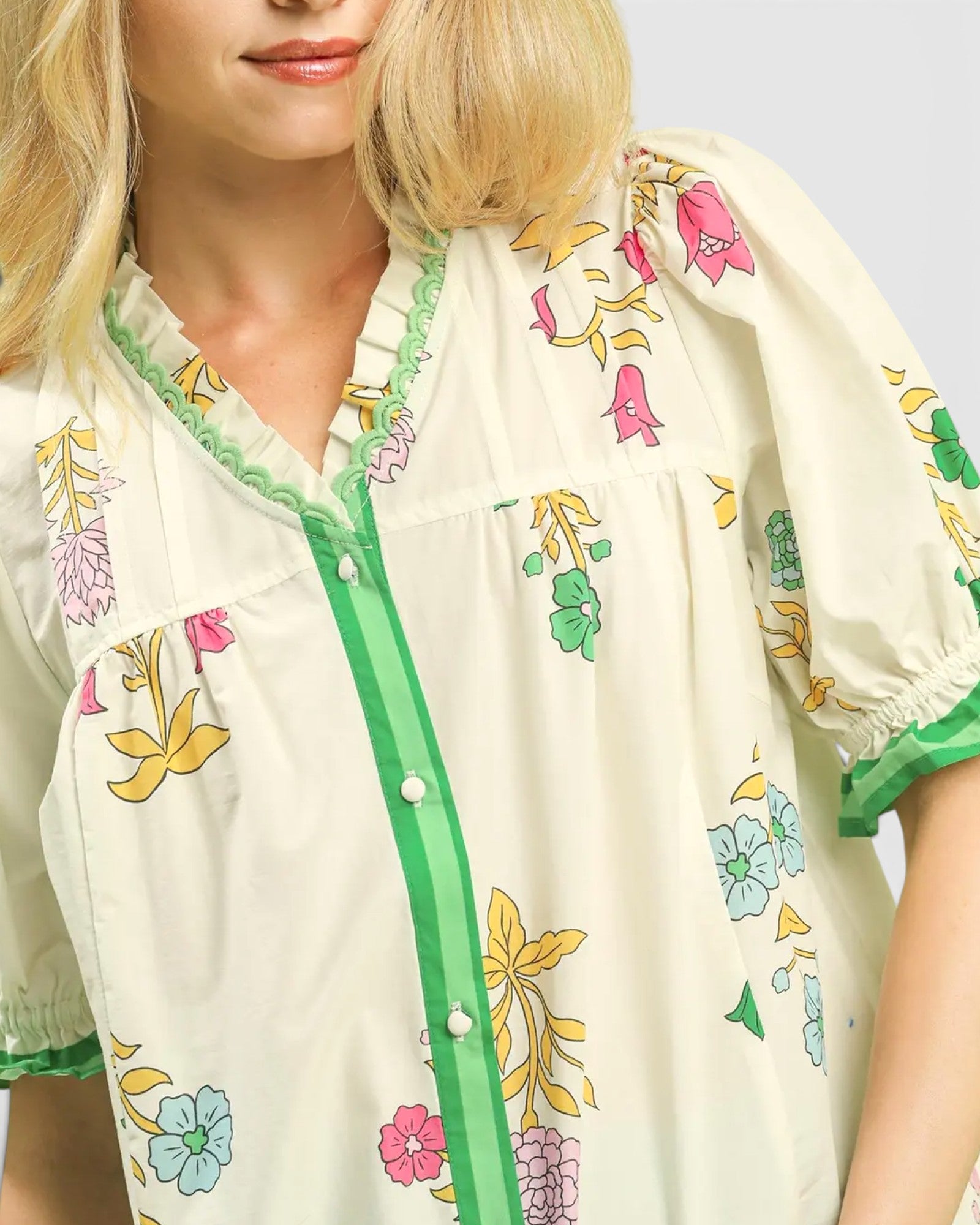 Woman wearing a floral blouse with green accents on a plain background