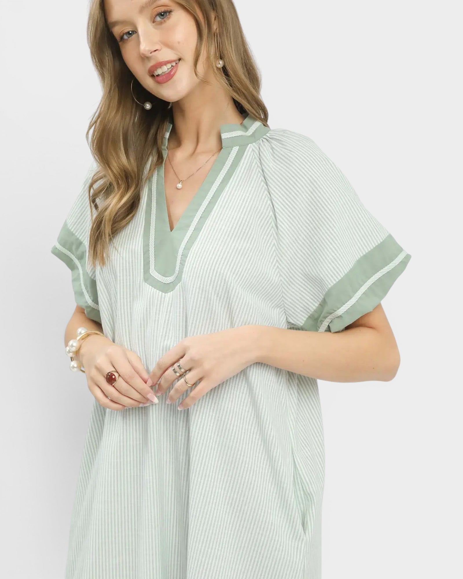 Woman wearing a light green dress with white stripes on a plain background