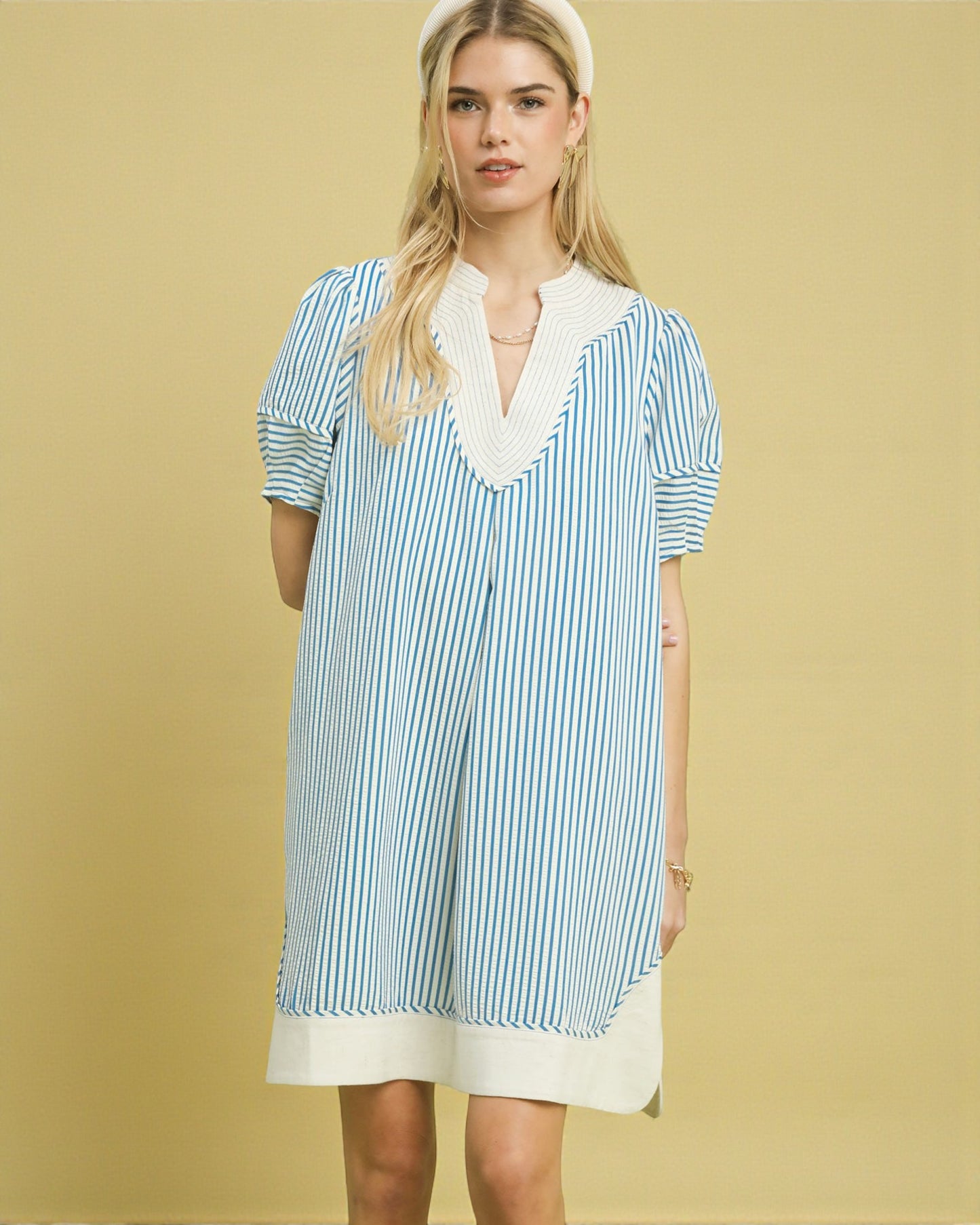 Woman wearing a blue and white striped dress with lace trim on a yellow background