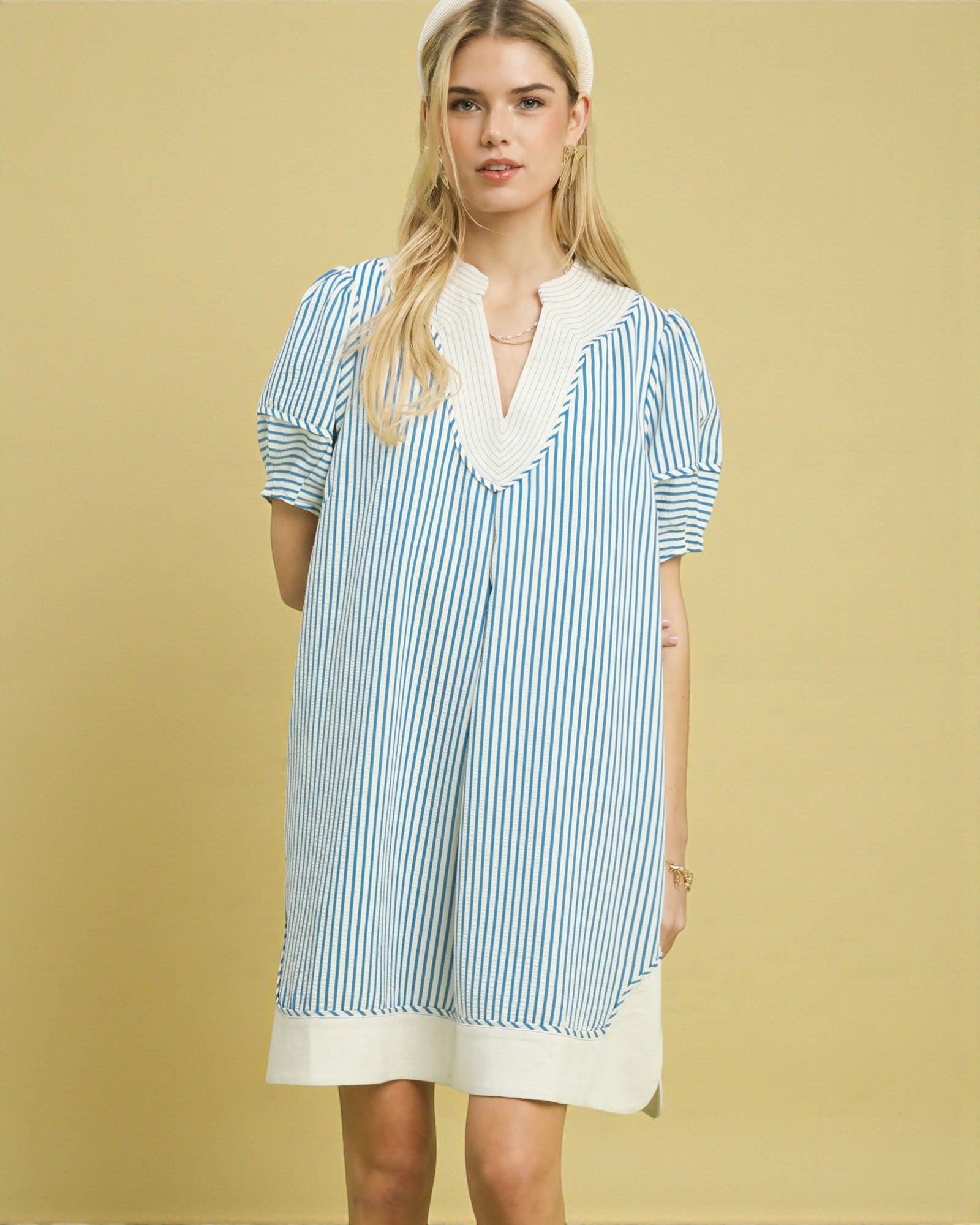 Woman wearing a blue and white striped dress with lace trim on a yellow background