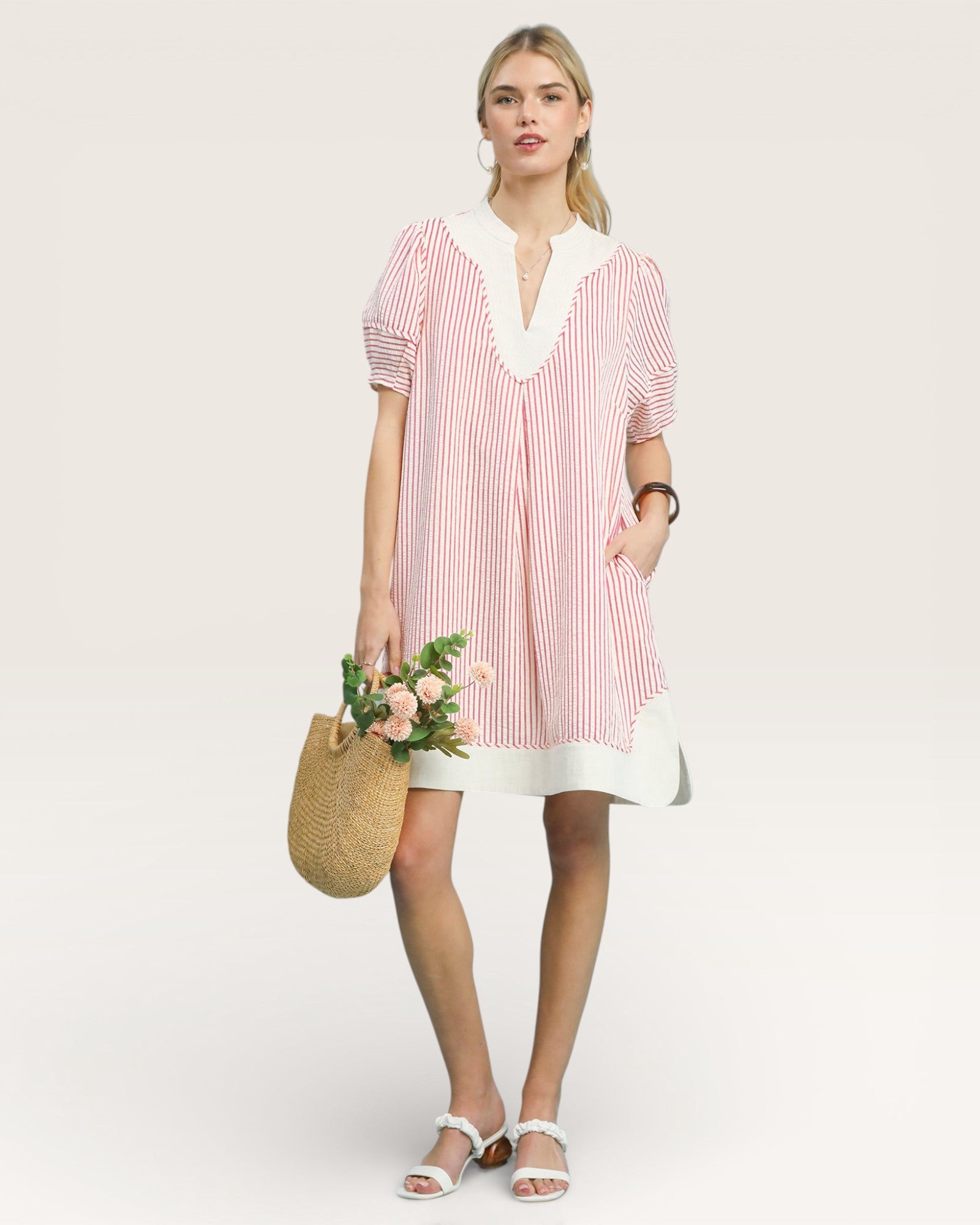 Woman wearing a pink and white striped dress holding flowers against a plain background