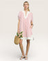 Woman wearing a pink and white striped dress holding flowers against a plain background