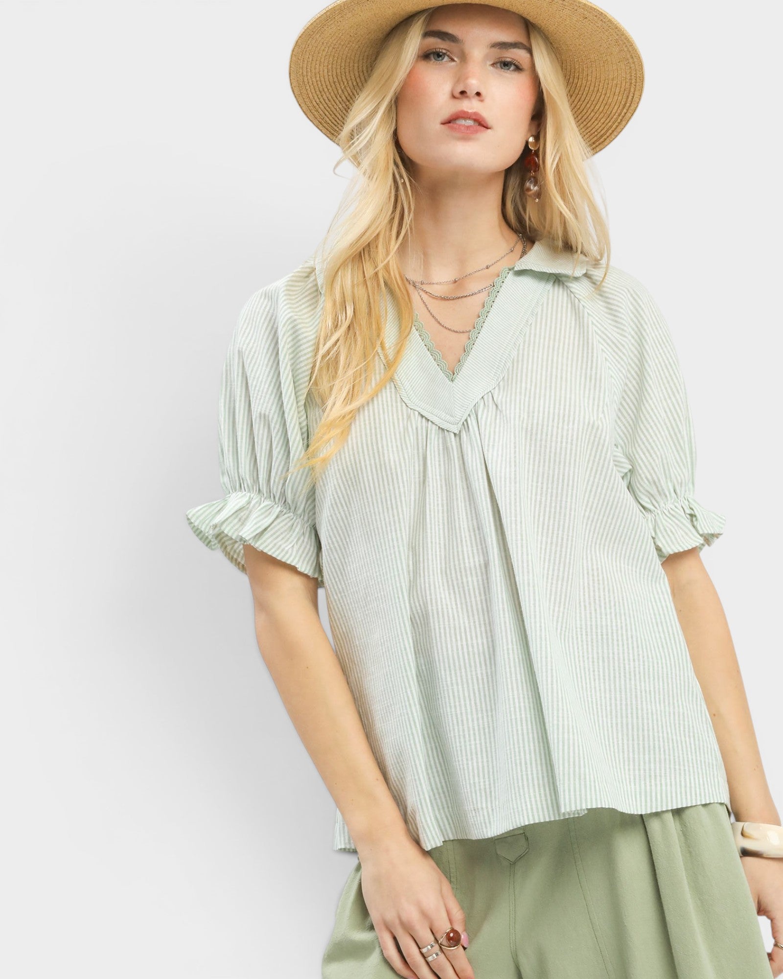 Woman wearing a light green blouse and beige hat against a white background