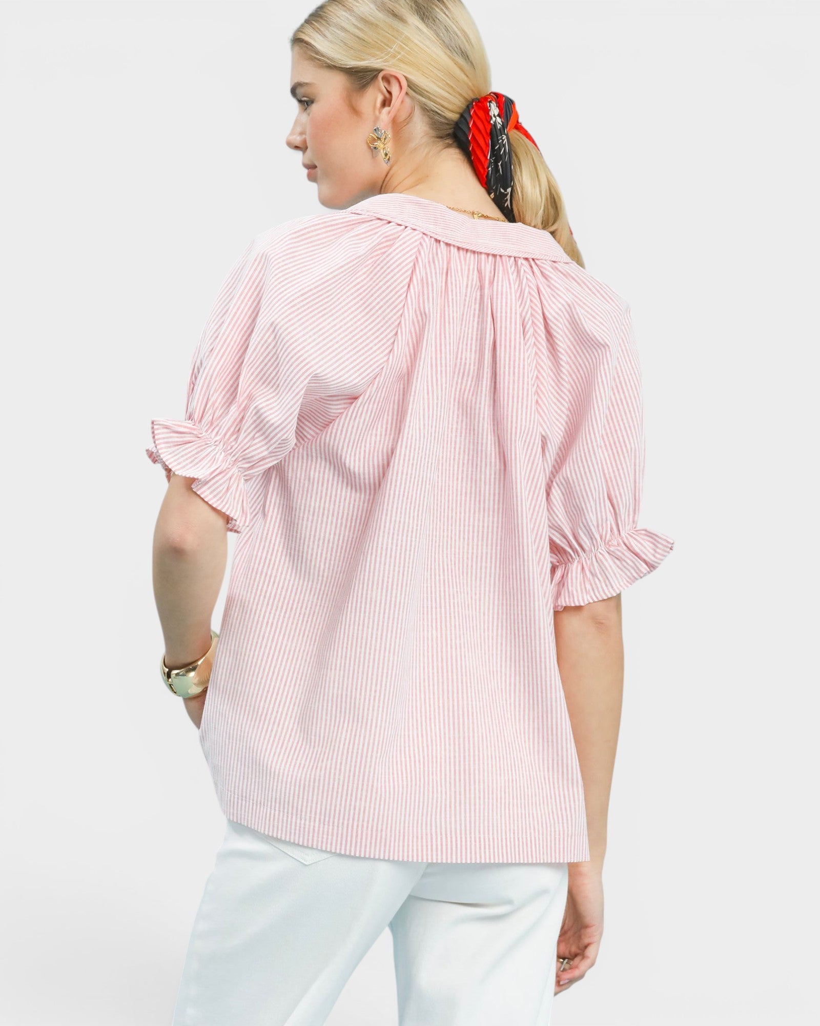 Woman wearing a pink striped blouse with ruffled sleeves on a white background