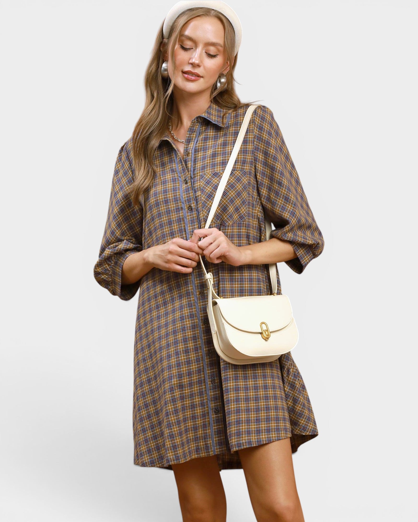 Woman wearing a plaid dress holding a beige handbag on a light gray background