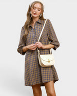 Woman wearing a plaid dress holding a beige handbag on a light gray background