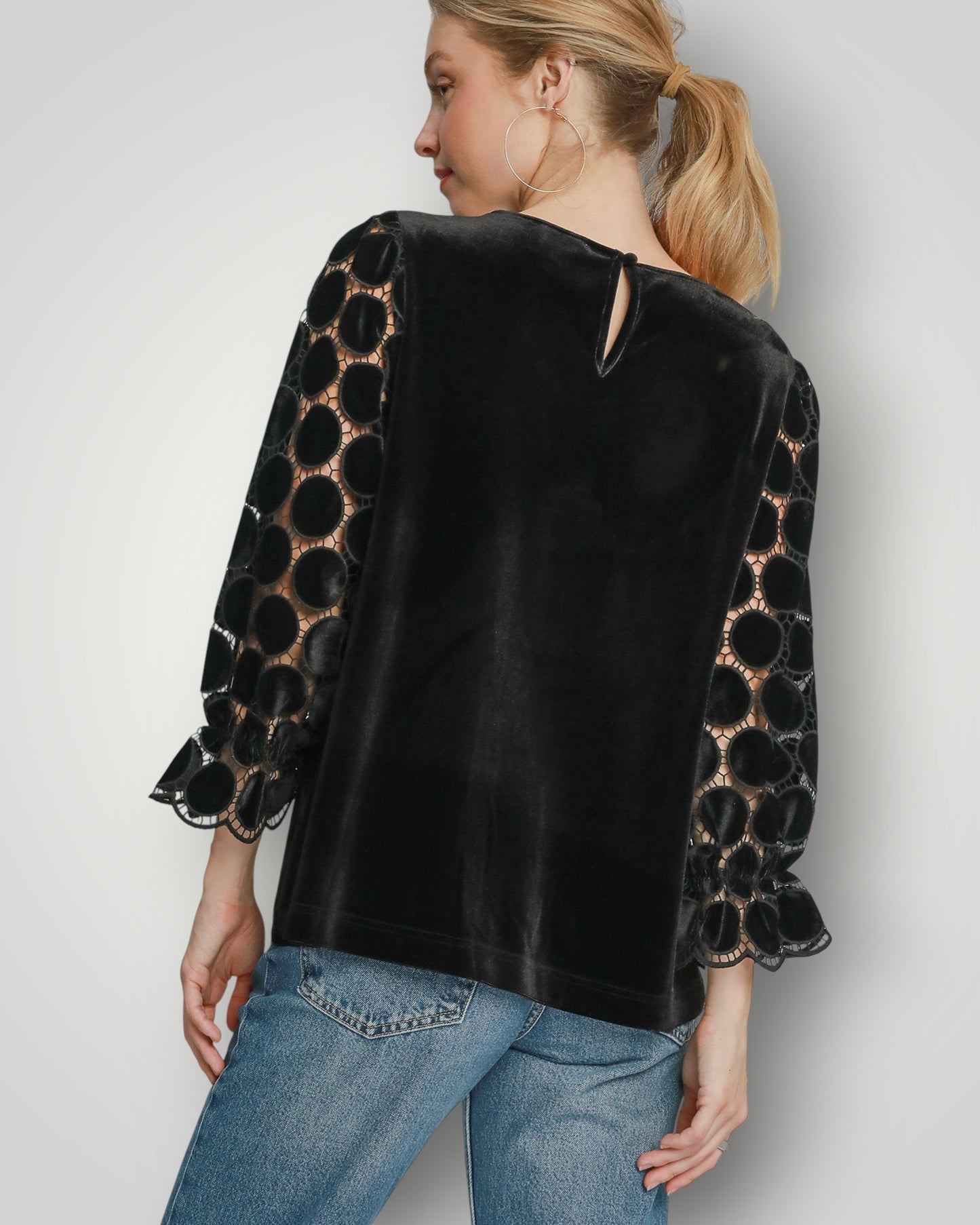 Woman wearing a black velvet top with patterned sleeves on a plain background