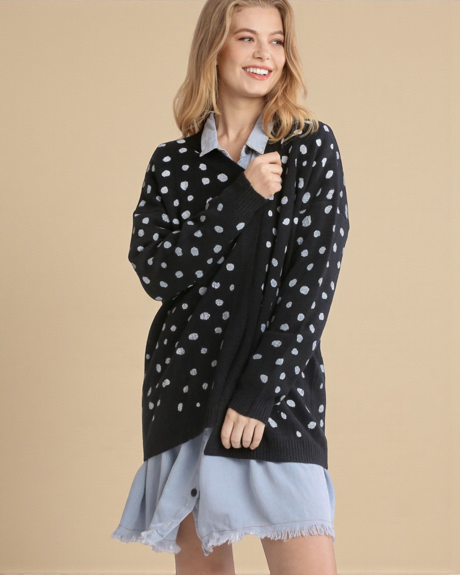 Woman wearing a black sweater with white polka dots over a light blue dress on a beige background
