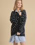 Woman wearing a black sweater with white polka dots over a light blue dress on a beige background