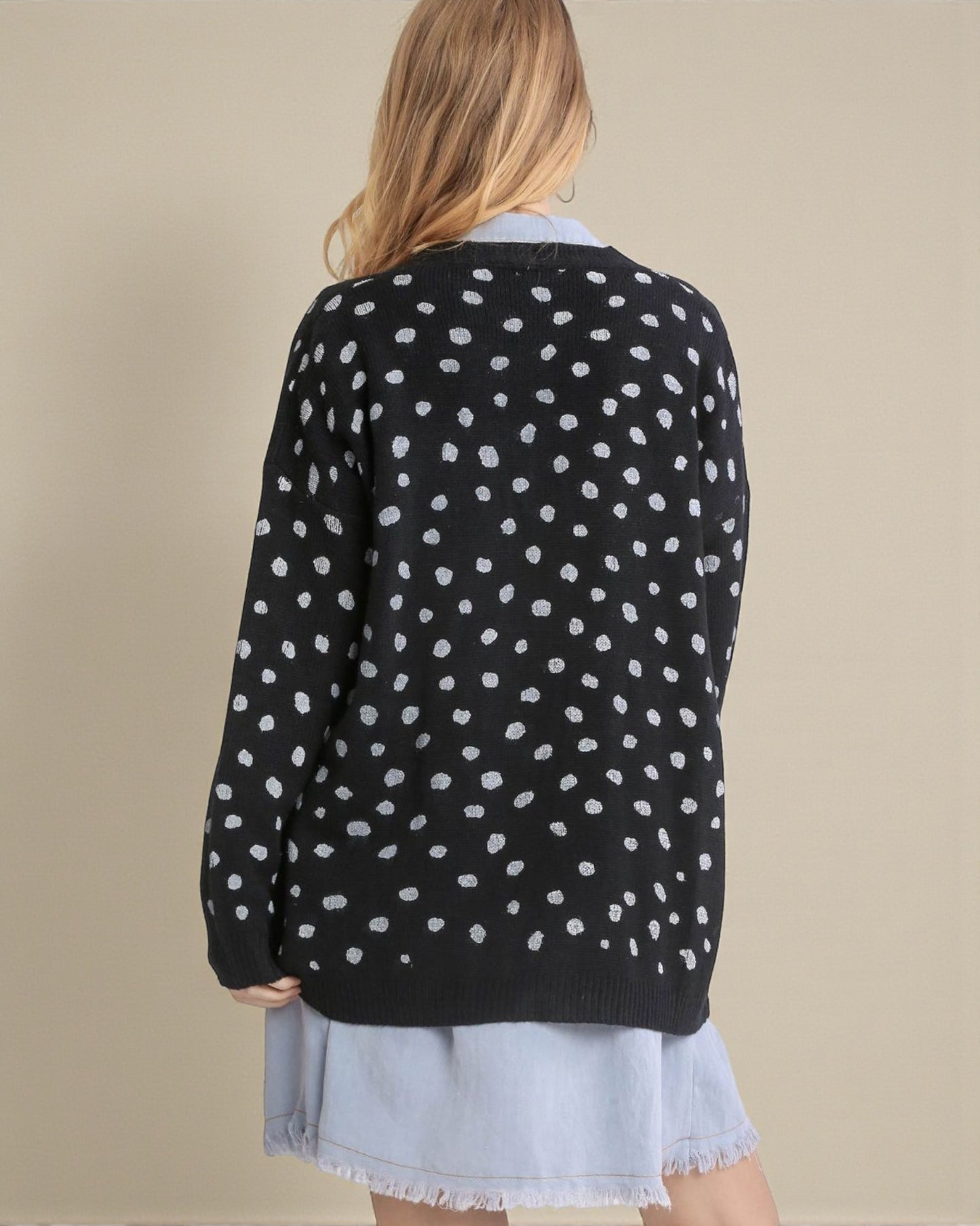 Person wearing a black sweater with white polka dots on a beige background