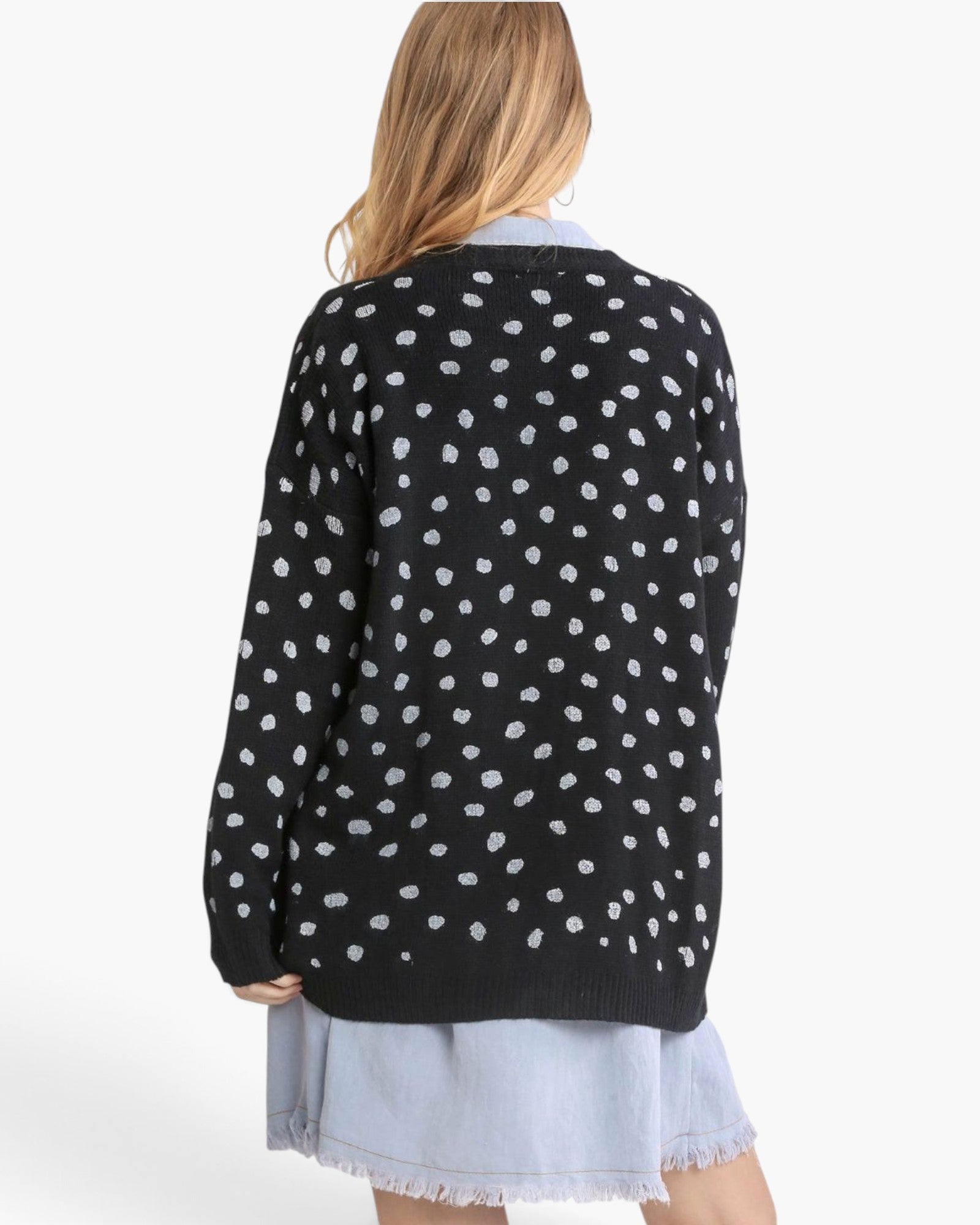 A woman shown from the back wearing a black knit cardigan with a white polka dot pattern, layered over a light blue denim skirt.