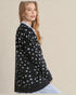 Woman wearing a black cardigan with white patterns on a beige background