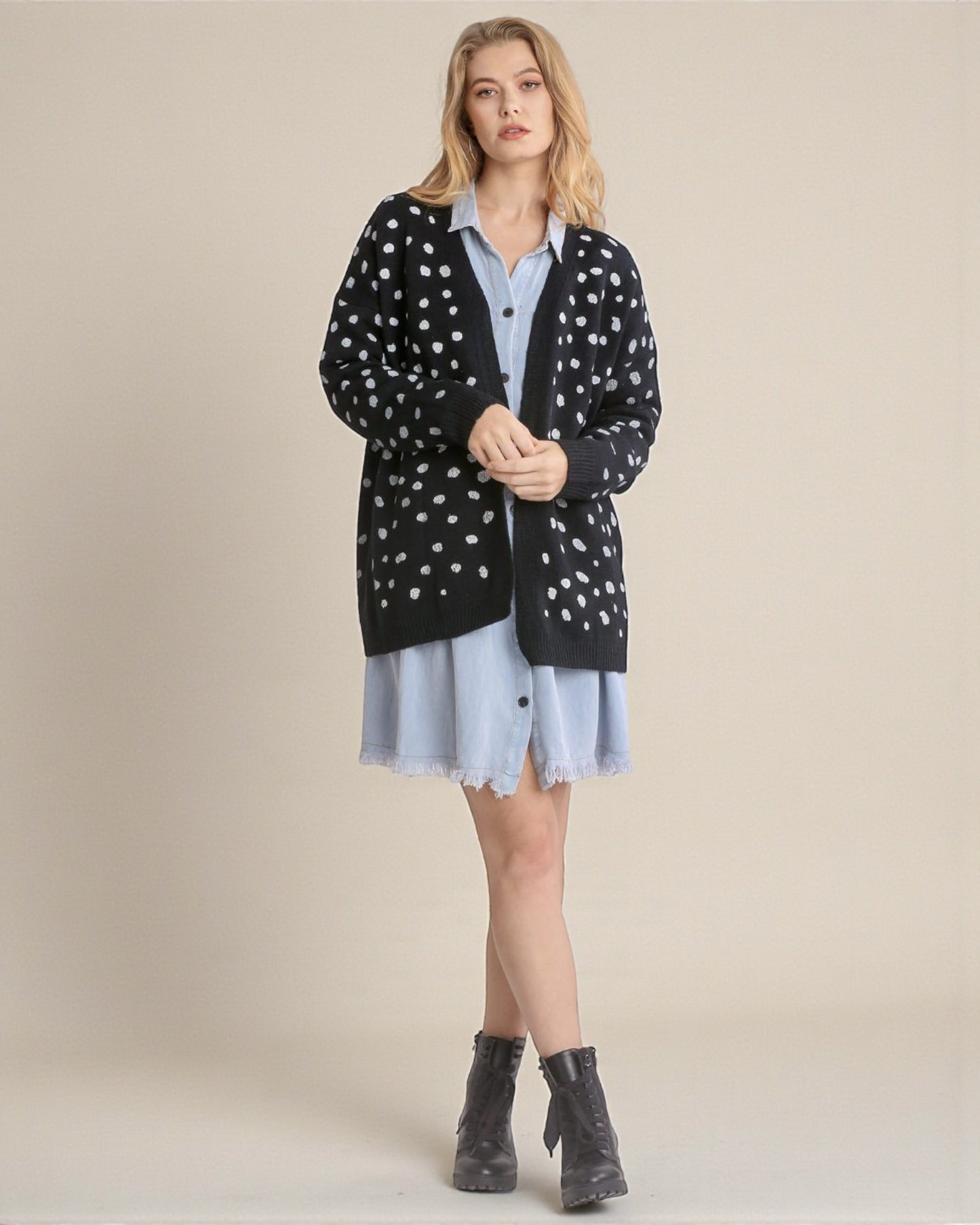 Woman wearing a black cardigan with white polka dots, light blue shirt, and skirt on a beige background