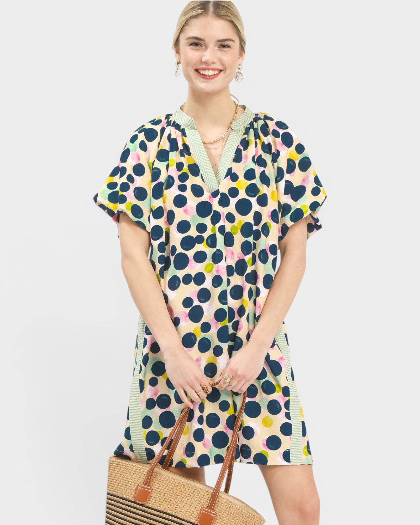 Woman wearing a patterned dress holding a straw bag on a plain background