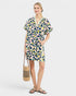 Woman wearing a patterned dress holding a straw bag on a white background