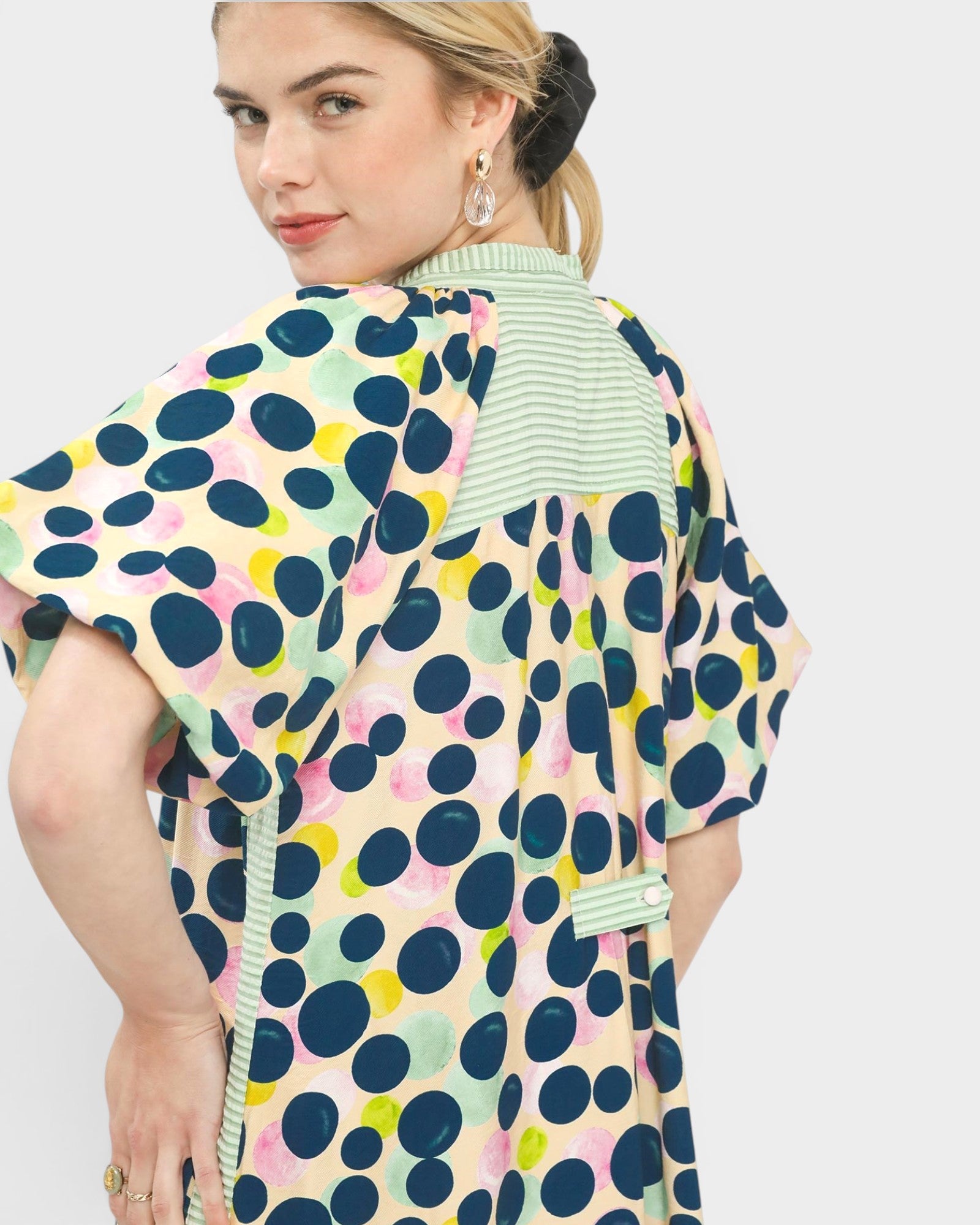 Woman wearing a colorful polka dot dress with a light green collar on a white background