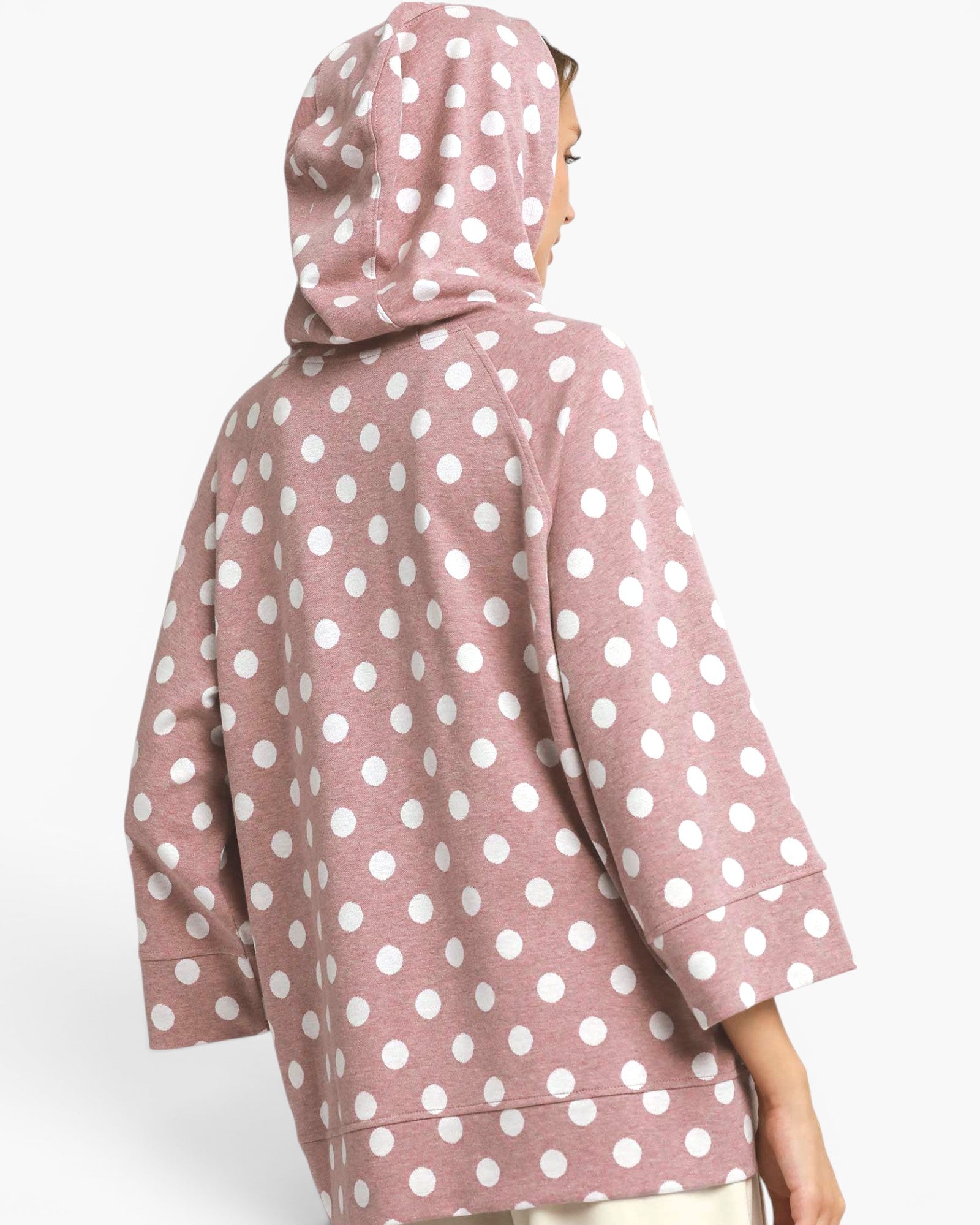 A person shown from the back wearing a dusty pink hooded sweatshirt with a white polka dot pattern, photographed against a light gray studio background.