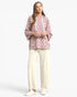 A woman modeling a dusty pink hooded sweatshirt with white polka dots and white drawstrings, paired with cream wide-leg pants and white sneakers, against a light gray studio background.