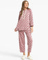 A woman modeling a two-piece pajama set featuring a dusty rose pink and white polka dot pattern, consisting of a hooded sweatshirt with white drawstrings and matching cropped pants, paired with white sneakers against a light gray background.