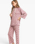 A woman modeling a matching two-piece pajama set with a dusty rose pink and white polka dot pattern, featuring a long-sleeve top with a drawstring hood and matching pants, set against a plain light gray background.