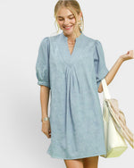 Woman wearing a light blue dress holding a beige bag on a white background