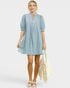 Woman wearing a light blue dress holding a beige bag on a white background