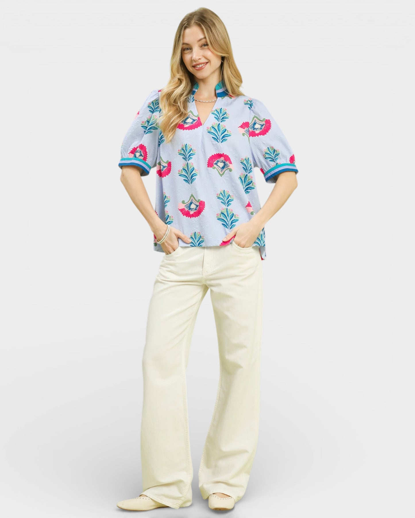 Woman wearing a colorful floral blouse and white pants on a white background