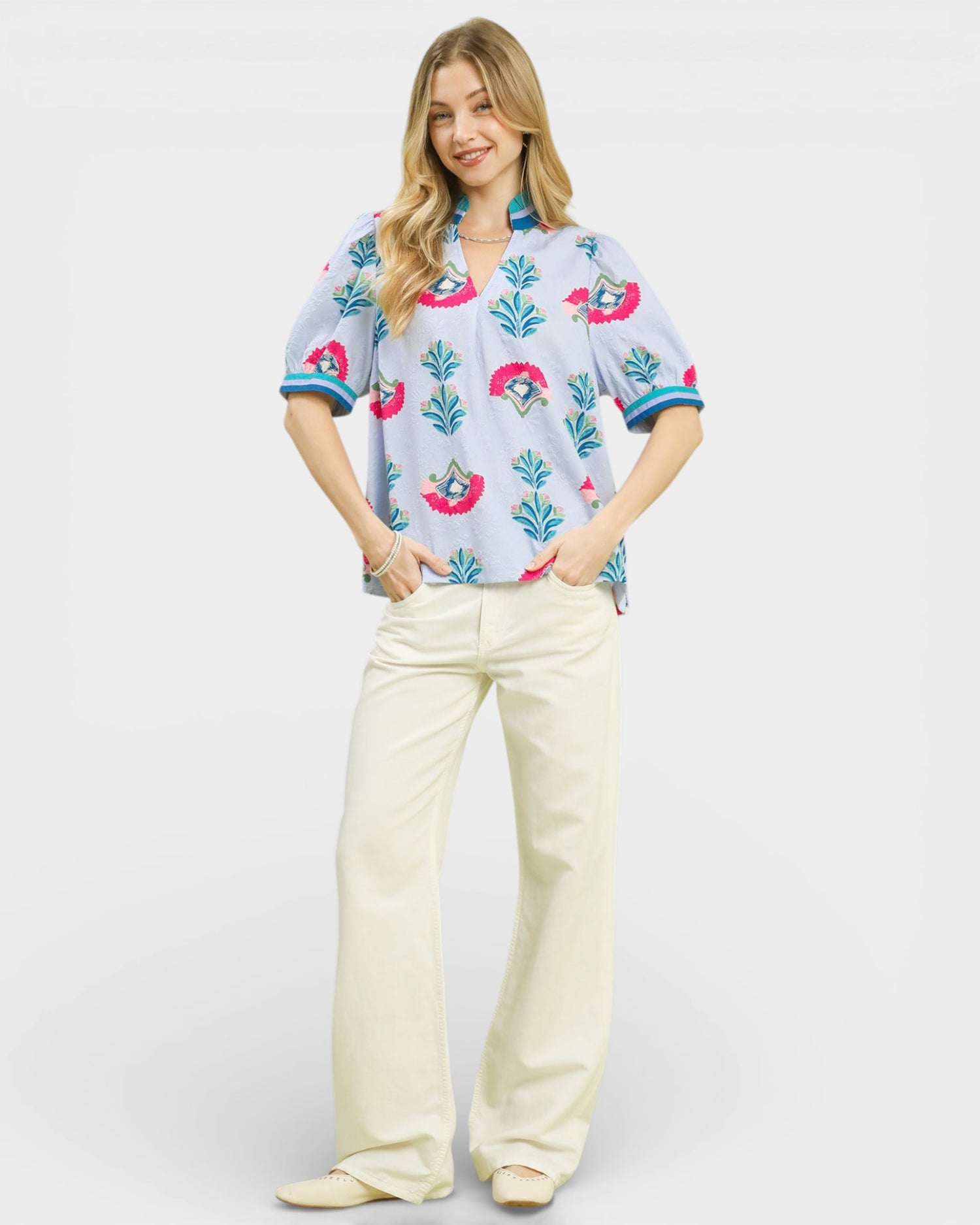 Woman wearing a colorful floral blouse and white pants on a white background